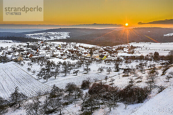 Drohnenansicht eines schneebedeckten Dorfes bei Sonnenuntergang im Winter