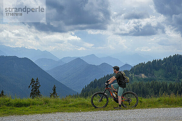Explorer looking at view while standing with mountain bike by path at Roßstein and Buchstein  Bavaria  Germany