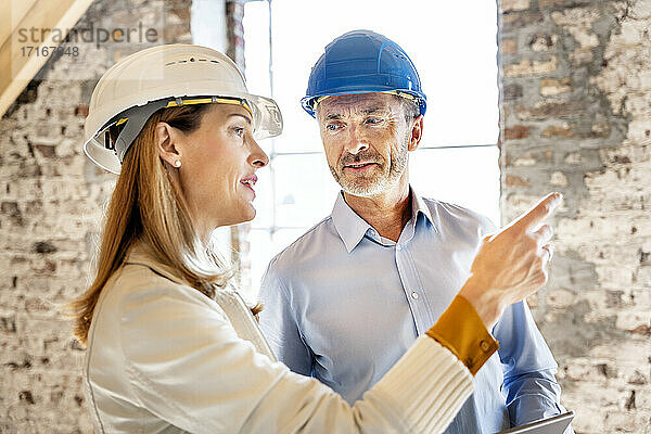 Geschäftsfrau mit Schutzhelm  die einem Bauunternehmer während der Arbeit auf der Baustelle Anweisungen gibt
