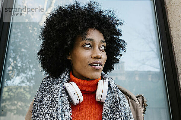 Afro-Frau mit Kopfhörern  die nachdenklich gegen eine Glaswand lehnt