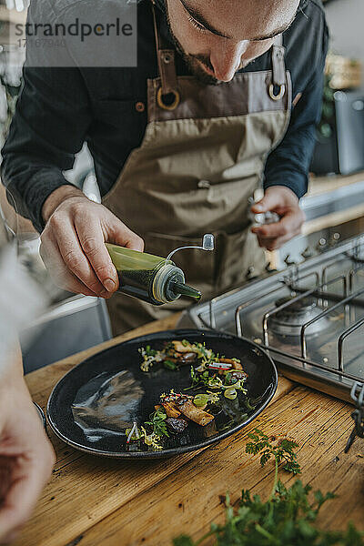 Male expertise garnishing sauce on cooked food while standing in kitchen