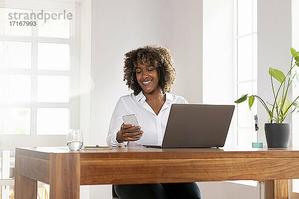 Unternehmer mit Laptop und Mobiltelefon im Home Office sitzend
