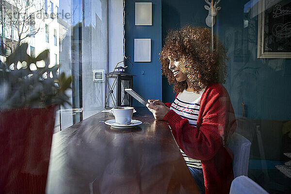 Woman smiling while using digital tablet sitting at cafe