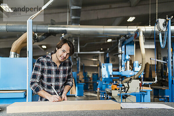 Smiling expertise measuring wood while working at industry