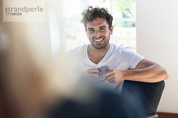 Mann mit Kaffeetasse lächelt  während er eine Frau zu Hause betrachtet