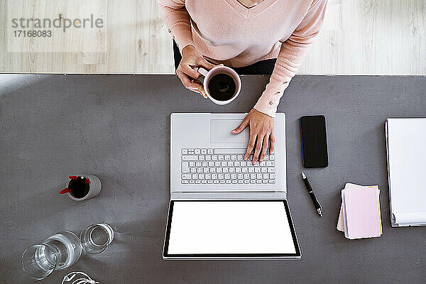 Young woman having coffee while using laptop while sitting at home