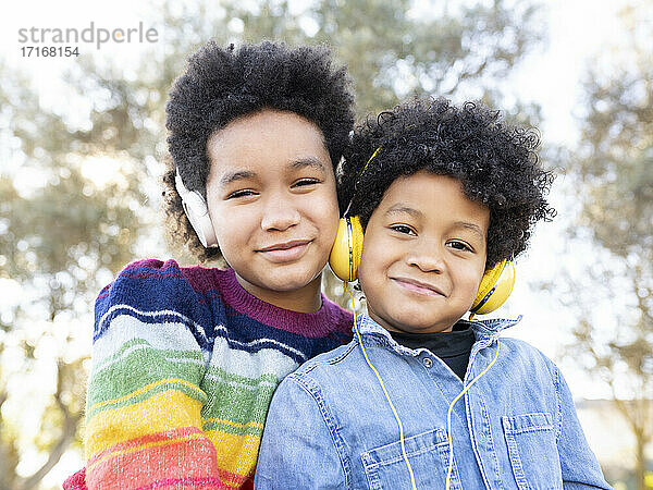 Bruder und Schwester tragen Kopfhörer und lächeln  während sie zusammen im Park sitzen