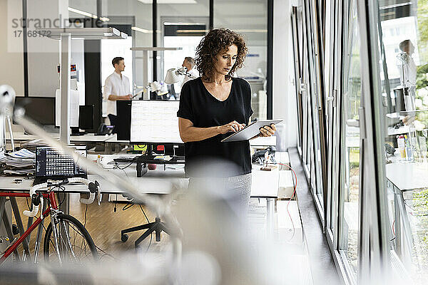 Geschäftsfrau  die ein digitales Tablet benutzt  während sie mit einem Kollegen im Hintergrund in einem Großraumbüro arbeitet