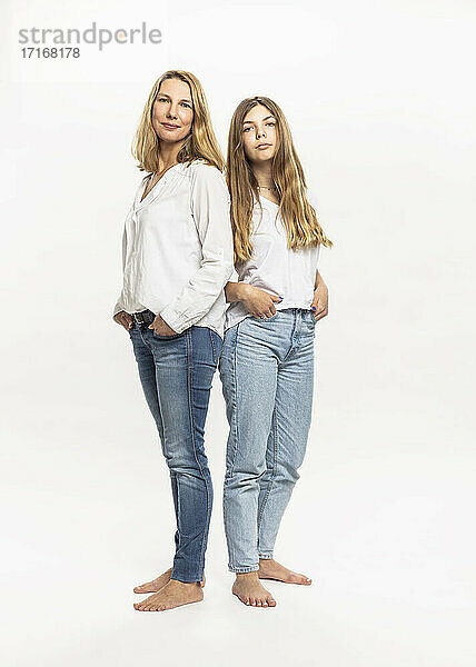 Mother and daughter with hands in pockets standing against white background