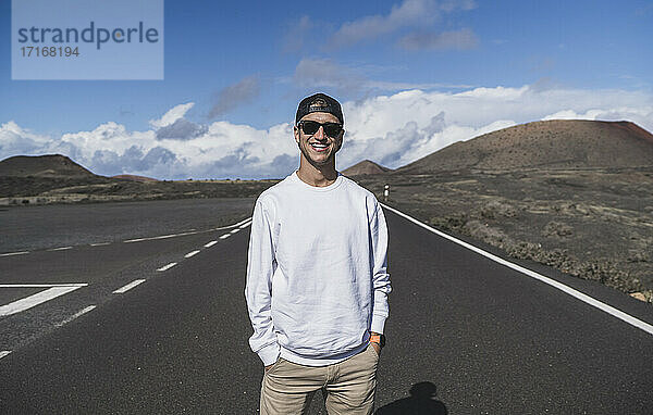 Lächelnder männlicher Tourist mit Händen in den Taschen vor dem Vulkan El cuervo in Lanzorte  Spanien