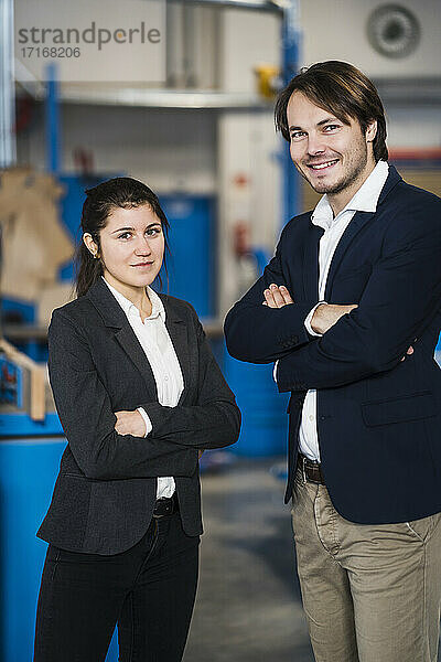 Young confident business people smiling while standing with arms crossed at industry