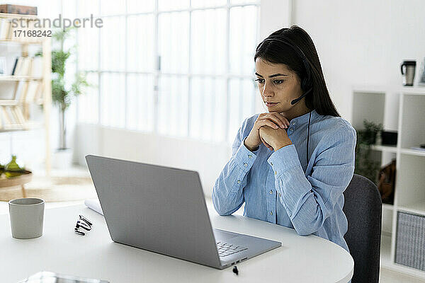 Geschäftsfrau mit Headset und Laptop im Sitzen mit Hand am Kinn im Büro