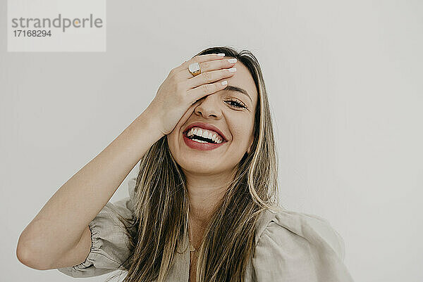 Smiling woman with hand covering eye against white background