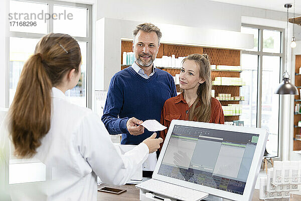 Male customer giving prescription list to female pharmacist at pharmacy checkout