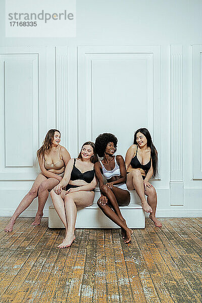 Glückliche multiethnische Gruppe von Modemodellen in Dessous vor weißer Wand