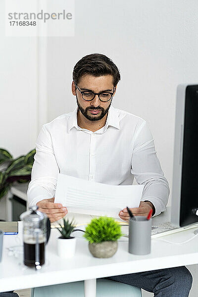 Männlicher Unternehmer mit Brille prüft Papierdokument bei der Arbeit am Arbeitsplatz