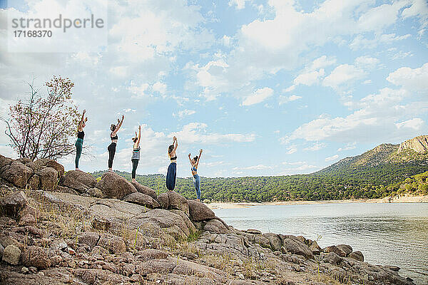 Junge Frauen üben Yoga mit Lehrer auf einem Felsen gegen den Himmel