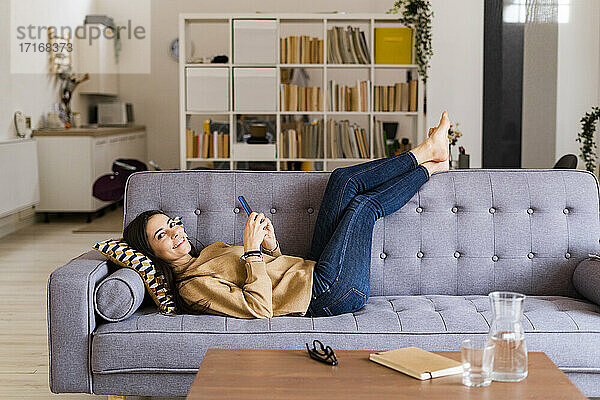 Smiling woman using smart phone while sitting on sofa at home