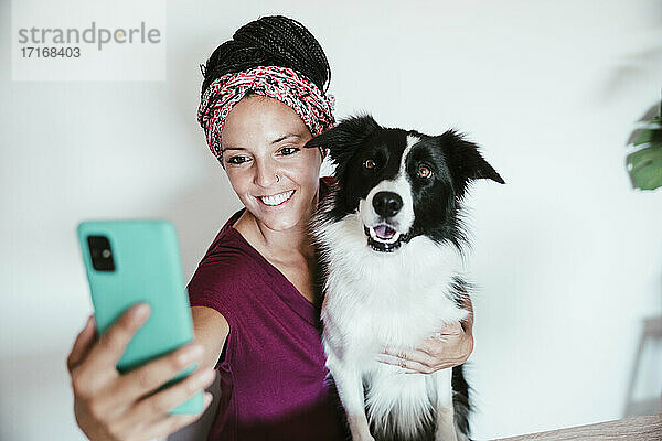 Lächelnde Frau macht Selfie mit Border Collie an der Hauswand