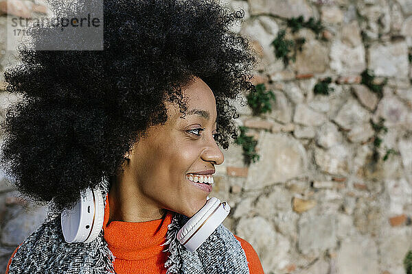 Glückliche Afro-Frau mit Kopfhörern  die gegen eine Steinmauer schaut
