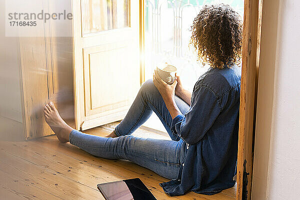 Curly woman with coffee cup sitting on floor at home