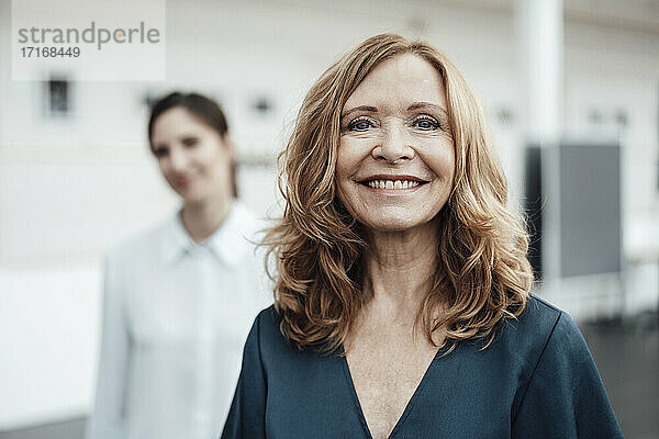 Lächelnde ältere Frau mit weiblicher Kollegin im Hintergrund im Büro