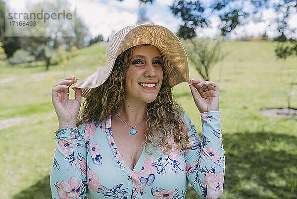 Smiling beautiful woman wearing sun hat in public park during sunny day