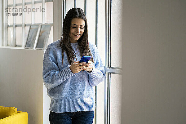 Smiling woman using smart phone while standing at home