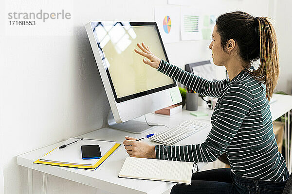 Kreative Geschäftsfrau berührt den Computerbildschirm bei der Arbeit im Büro
