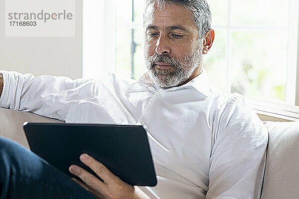 Geschäftsmann  der ein digitales Tablet benutzt  während er zu Hause auf dem Sofa sitzt