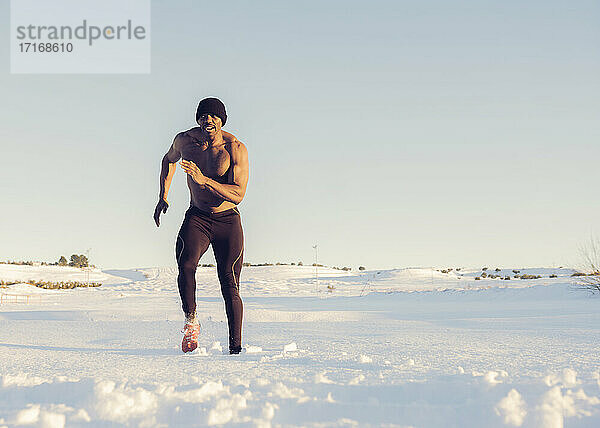 Sportler ohne Hemd beim Laufen im Schnee während des Sonnenuntergangs