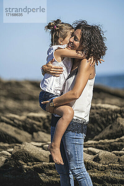 Mother embracing daughter while standing on flysch against sky