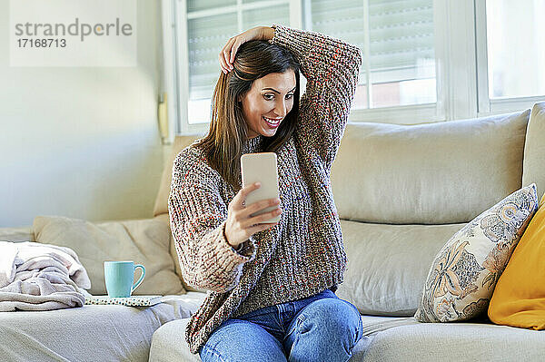 Smiling woman taking selfie on sofa at home