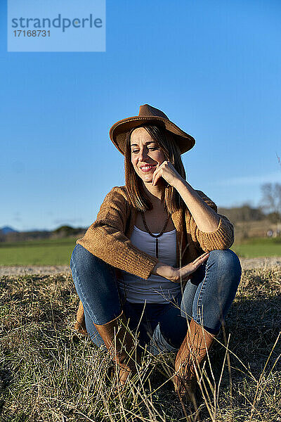 Woman with hand on chin looking down while sitting on land against blue sky