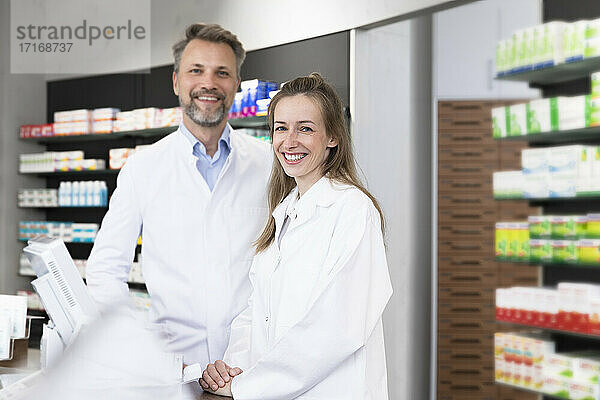 Smiling female pharmacist with male coworker at checkout in store