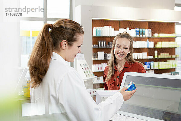 Female pharmacist reading instructions on medicine while woman standing at checkout