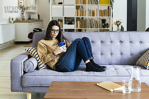 Young woman using mobile phone while sitting resting on sofa at home
