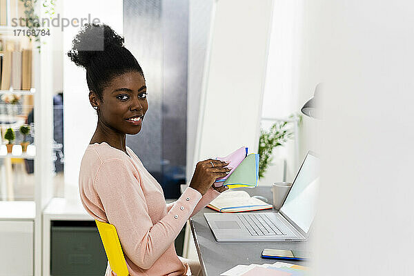 Lächelnde Geschäftsfrau  die ein buntes Stoffmuster hält  während sie zu Hause im Büro sitzt