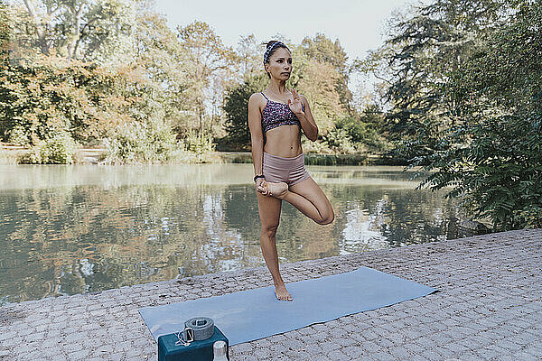 Sportswoman standing on one leg while practicing yoga by lake at park