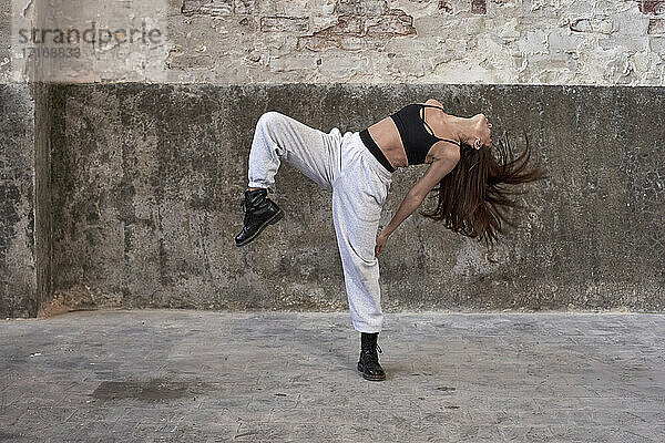 Female dancer dancing while hair tossed against wall in abandoned factory