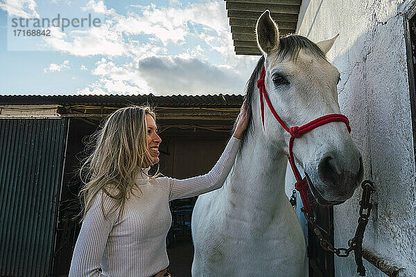 Smiling woman consoling horse while standing against stable