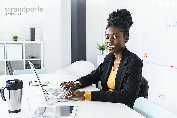 Young Afro businesswoman using laptop while sitting at desk in office