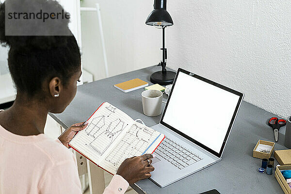 Modestylistin mit Laptop  die zu Hause sitzend ein Diagramm in einem Buch analysiert