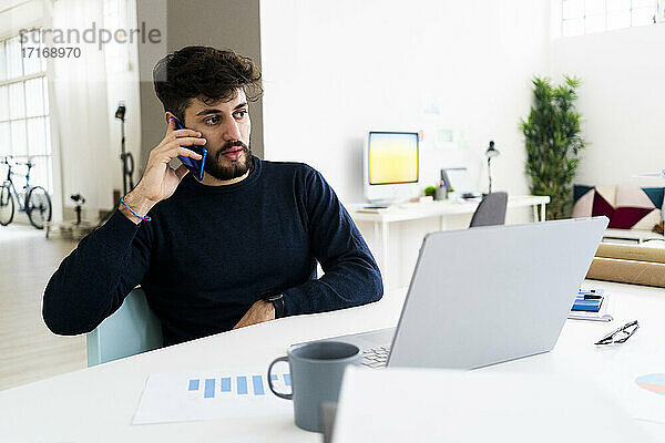 Junger Geschäftsmann  der in einem kreativen Büro am Telefon spricht