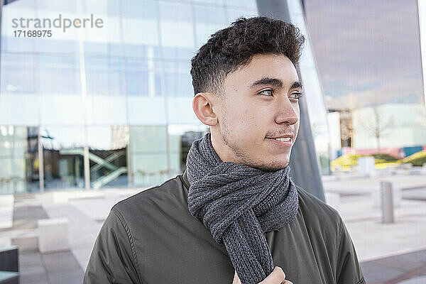 Lächelnder Mann mit Schal  der vor einem modernen Gebäude wegschaut