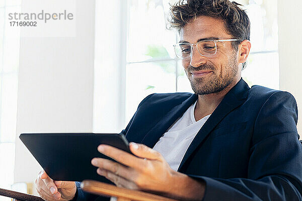Lächelnder Geschäftsmann  der ein digitales Tablet benutzt  während er zu Hause sitzt