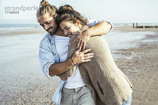 Lächelnde Freundin umarmt ihren Freund am Strand an einem sonnigen Tag