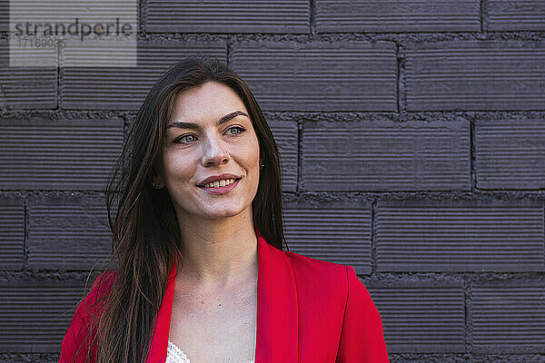 Beautiful smiling businesswoman with gray eyes looking away against brick wall