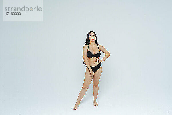 Übergroße junge Frau im schwarzen Bikini posiert vor weißem Hintergrund