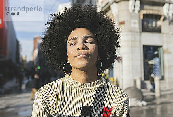 Afro woman with eyes closed standing in city